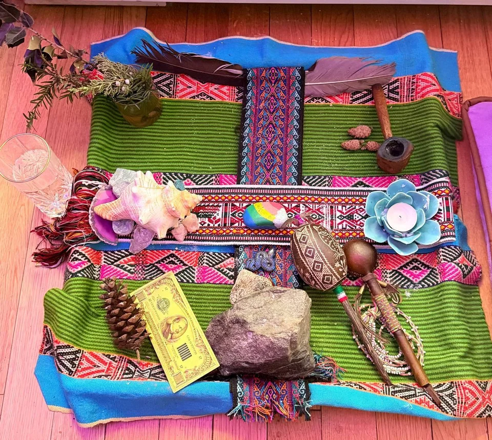 A mesa with stones, a shell, feathers, and a candle on woven textiles