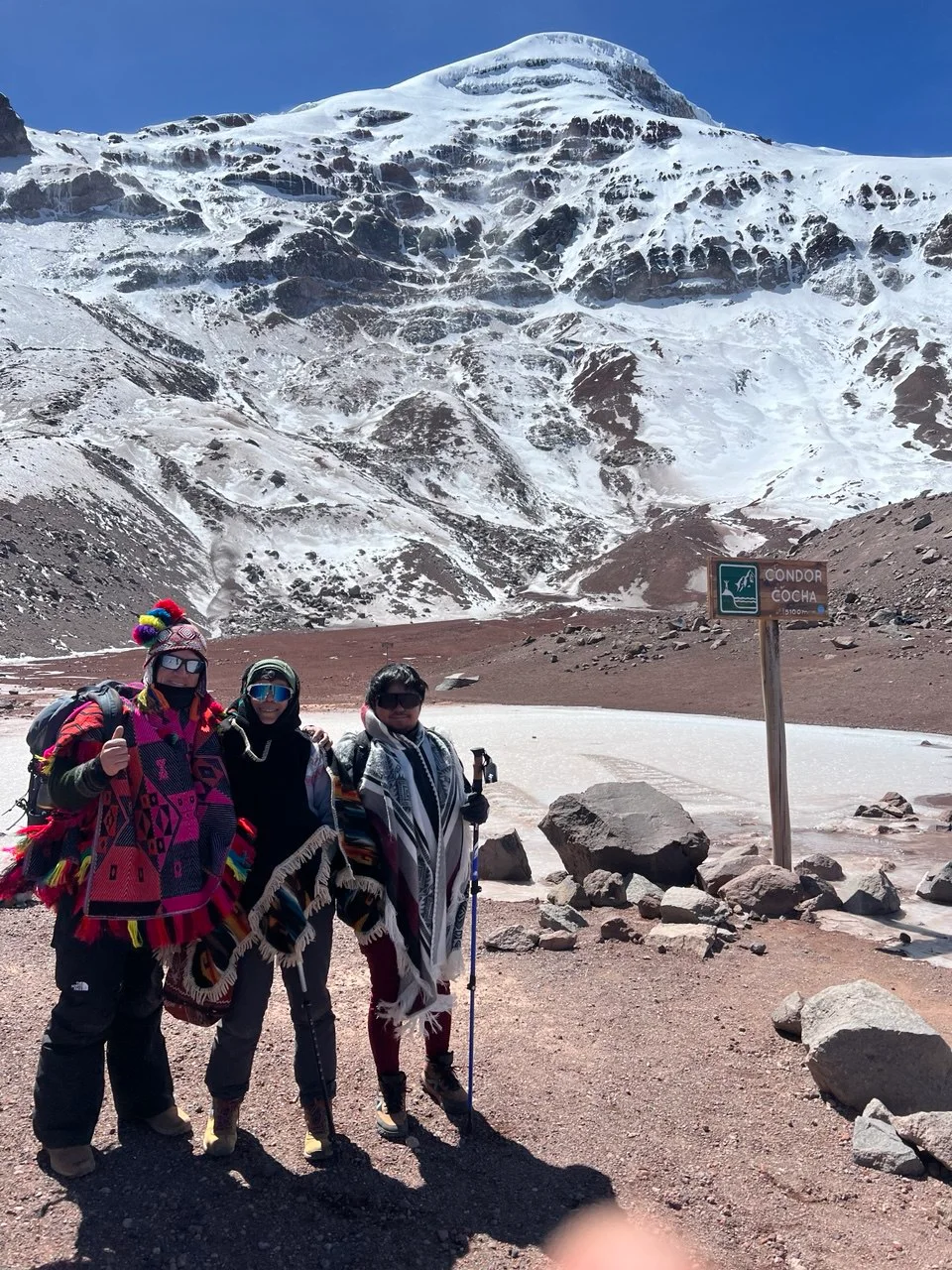 Three people gathered beneath a snow-covered mountain in the Andes